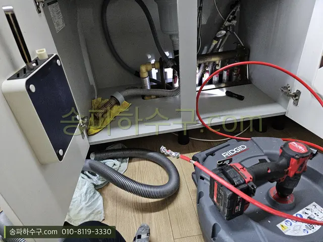 싱크대 하부장 안에서 배관 장비로 작업하는 모습